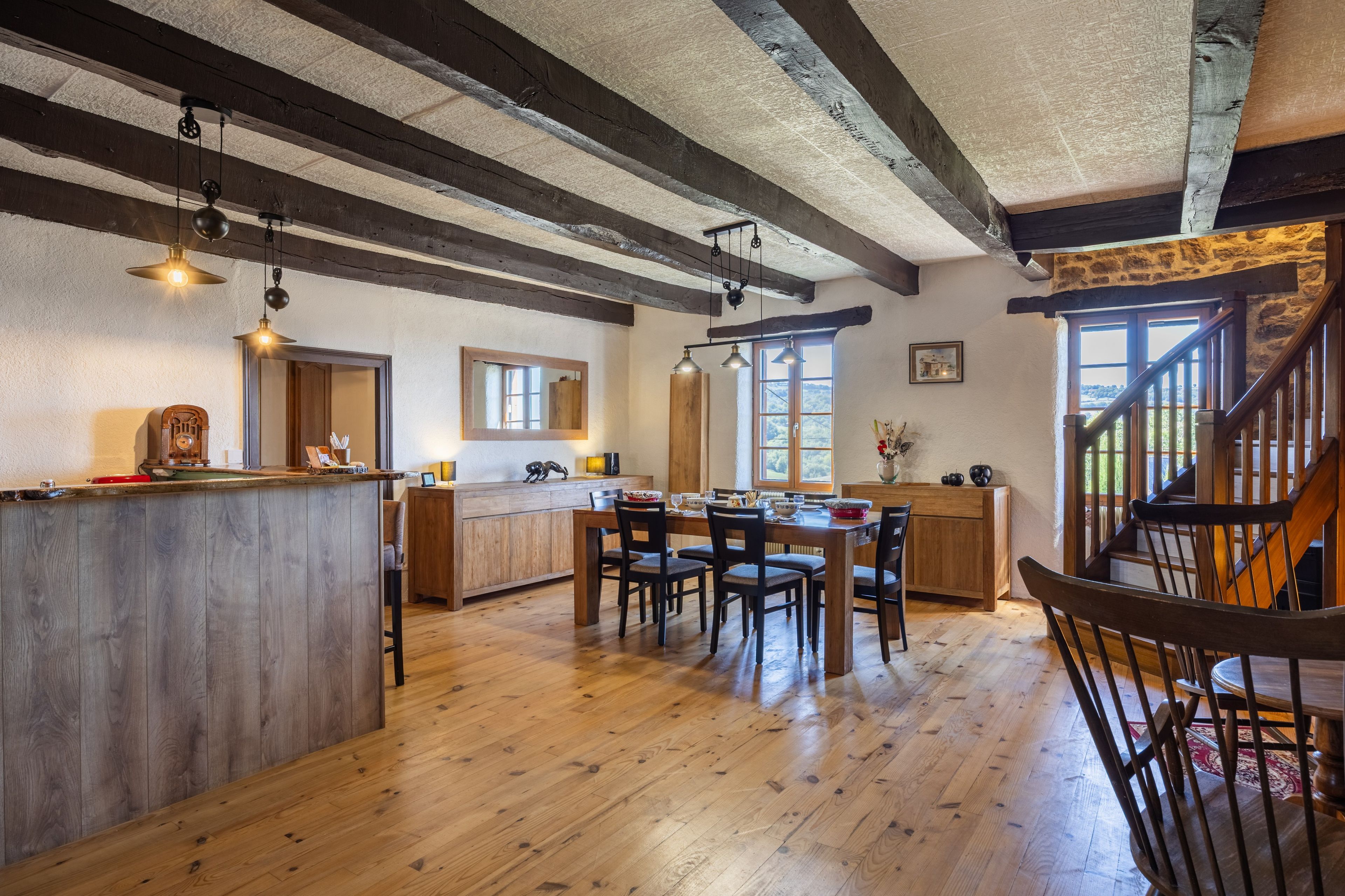 A spacious kitchen with wooden beams, a central island, and a dining area with chairs and a table.