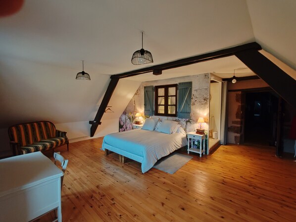 A bedroom with a sloped ceiling, a bed, a chair, bedside tables, and hanging lights. - Sans Chichi Chambres et Table: Mountain View, Shared Terrace & Wi-Fi (Escandolières)
