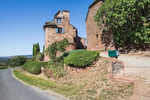 Un bâtiment en pierre avec une petite tour, une boîte aux lettres et une route qui tourne vers la gauche.