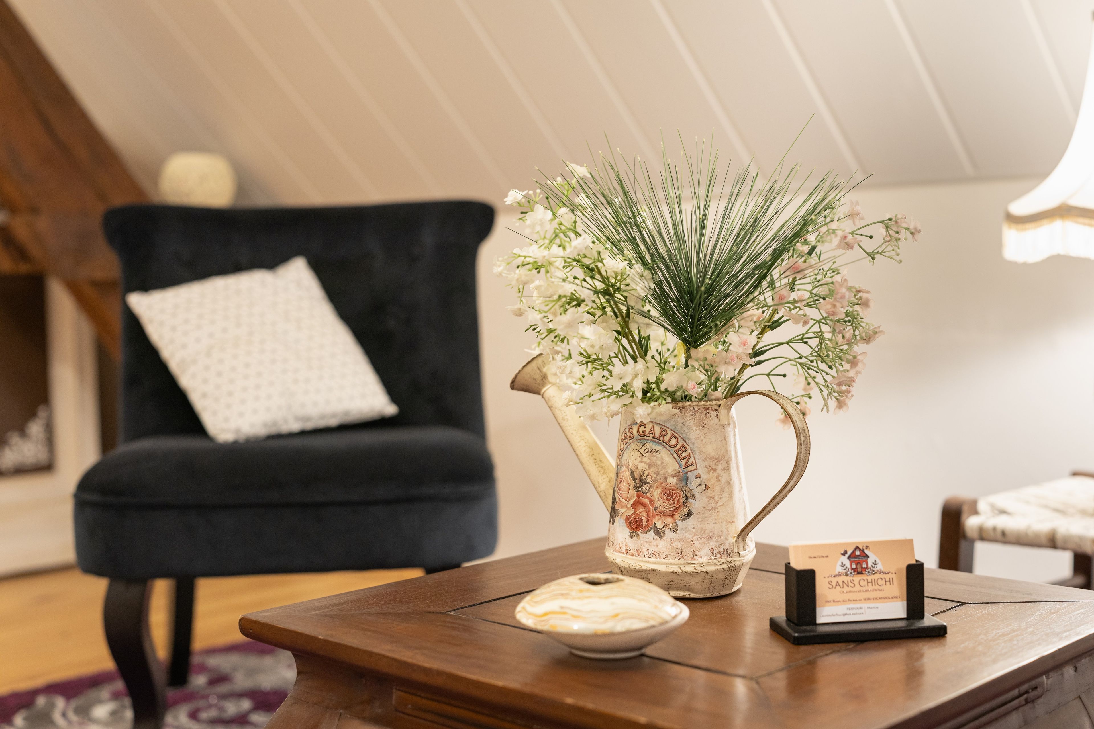 A wooden table with a vase of flowers, a small bowl, and a business card.