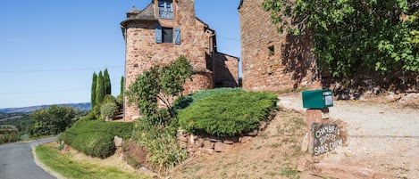A stone building with a small tower, a mailbox, and a road curving to the left.