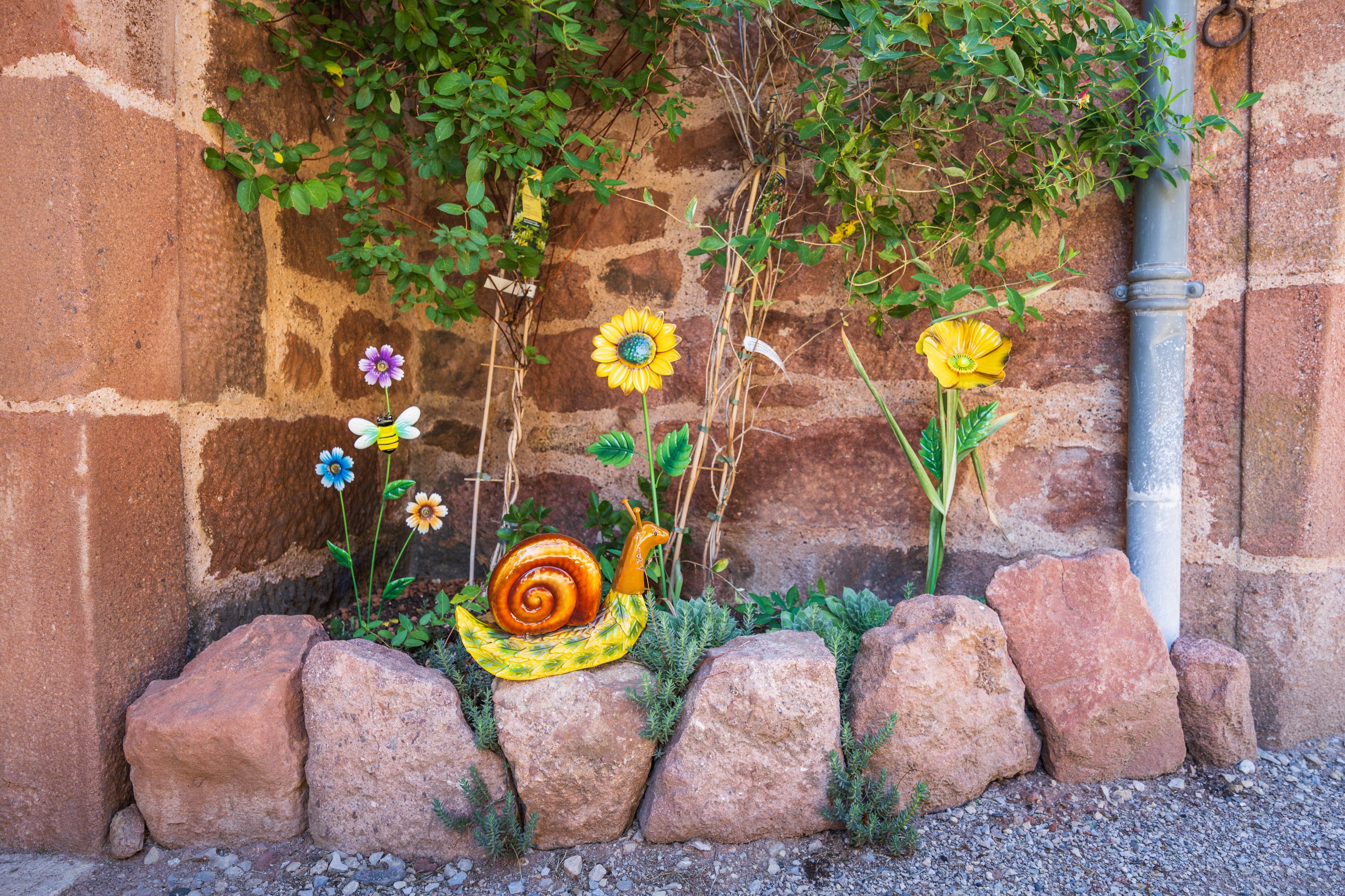 A garden wall with a snail sculpture, various flowers, and climbing plants.