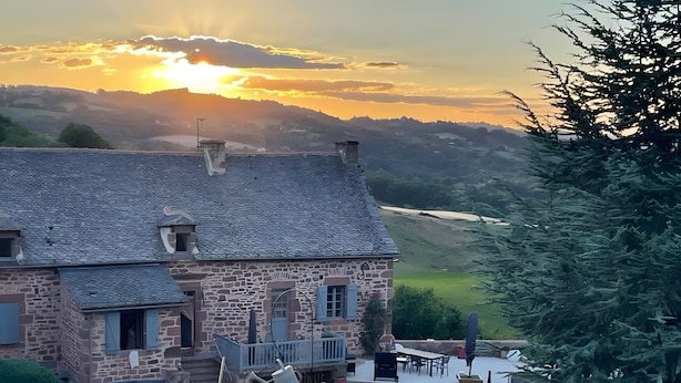 Ein Steinhaus mit Balkon, eine Terrasse mit Gartenmöbeln und Blick auf ein Tal.