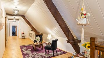 Une pièce de style loft avec des poutres en bois, un fauteuil noir, une table en bois et un luminaire suspendu en macramé.