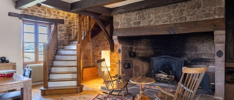A rustic interior with a stone fireplace, wooden staircase, and a dining area.