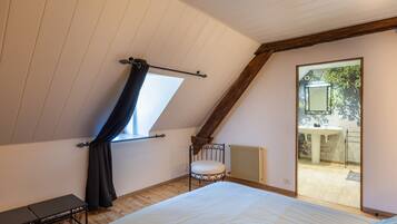 A bedroom with a sloped ceiling, a bed, a small table, a chair, and a window with curtains.