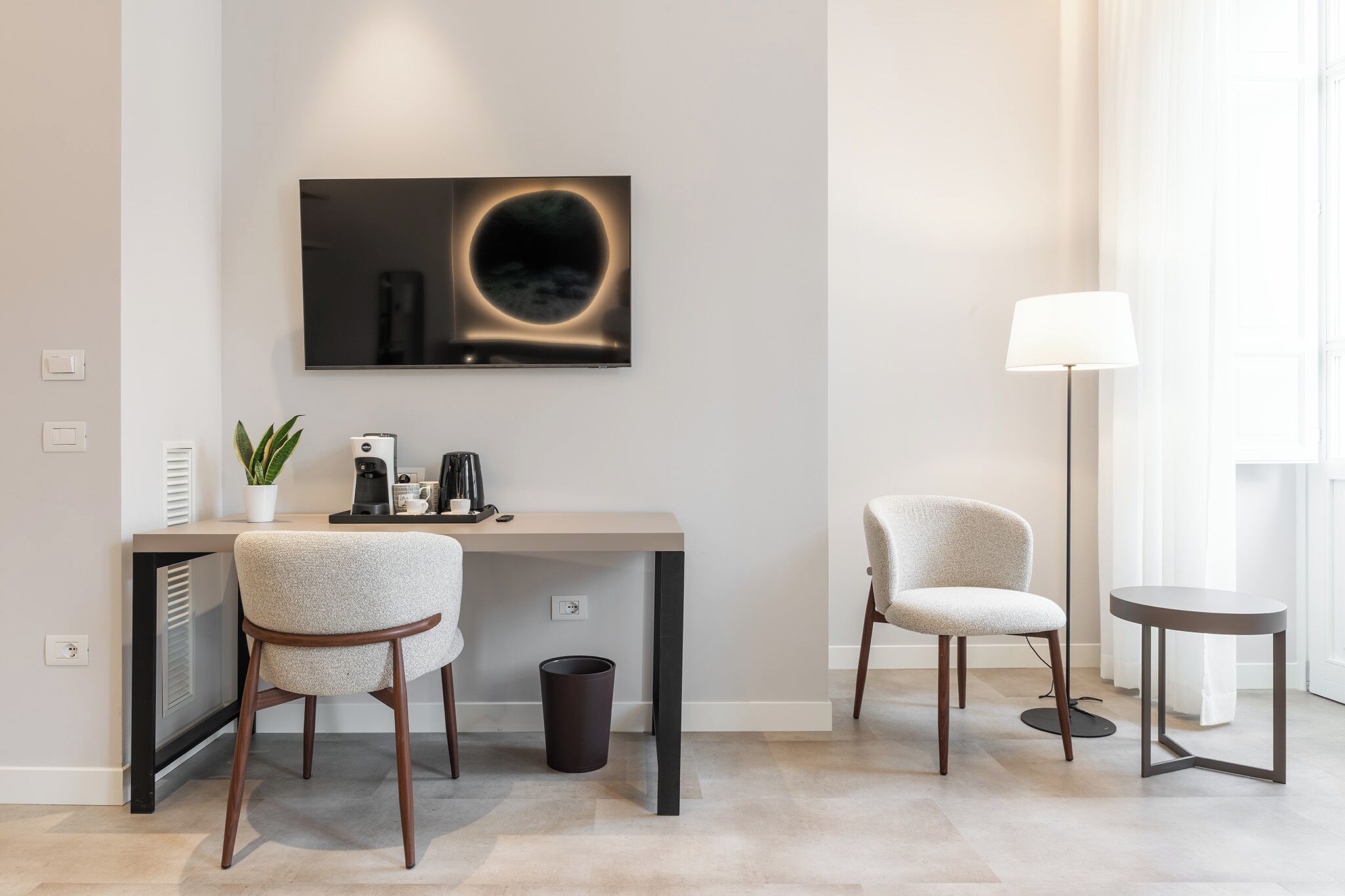 Une chambre moderne équipée d’un bureau, de deux chaises, d’une machine à café, d’une poubelle et d’un lampadaire.