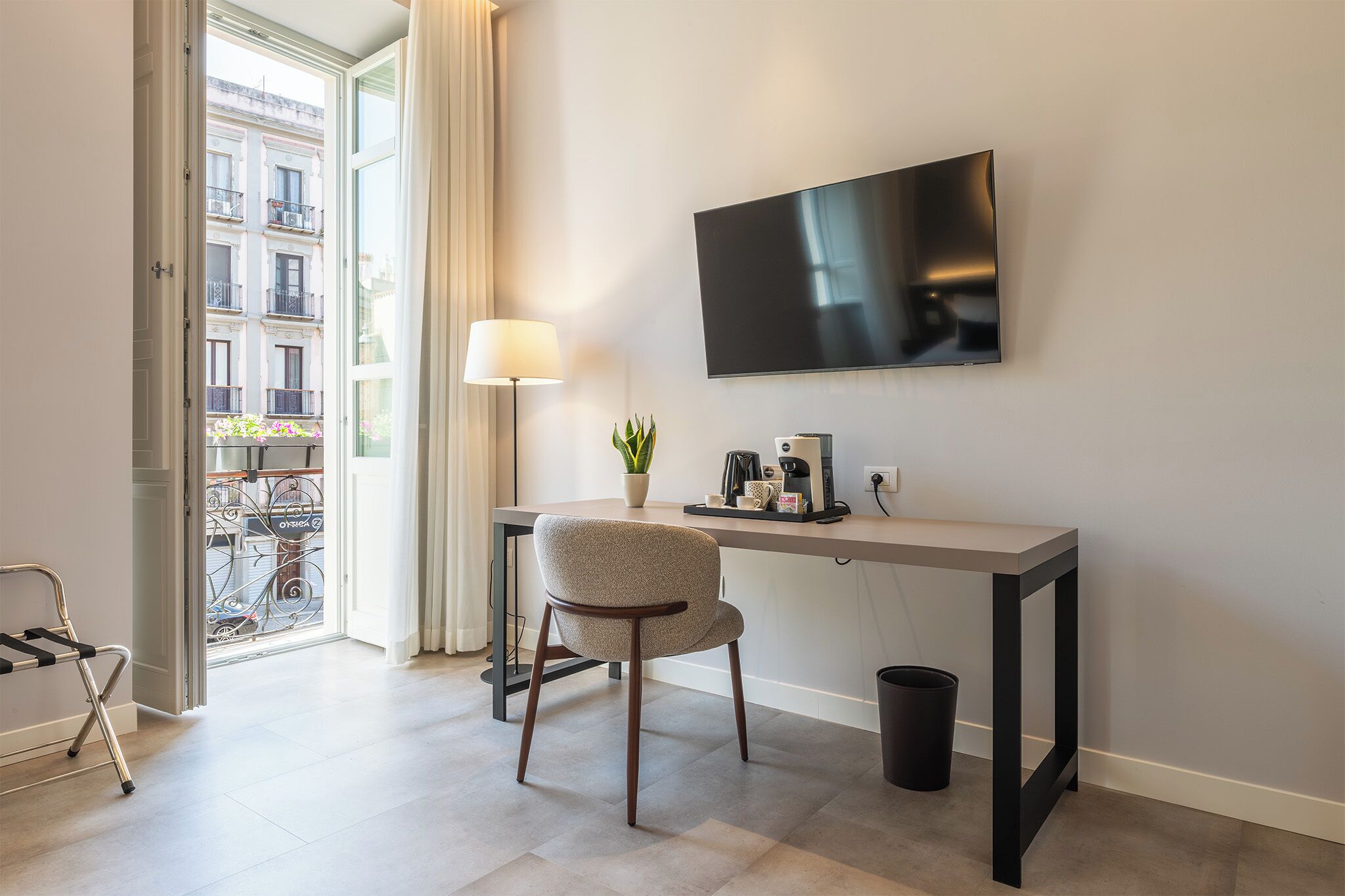 Ein Hotelzimmer mit Schreibtisch, Stuhl, Fernseher, Lampe und Blick auf die Straße.