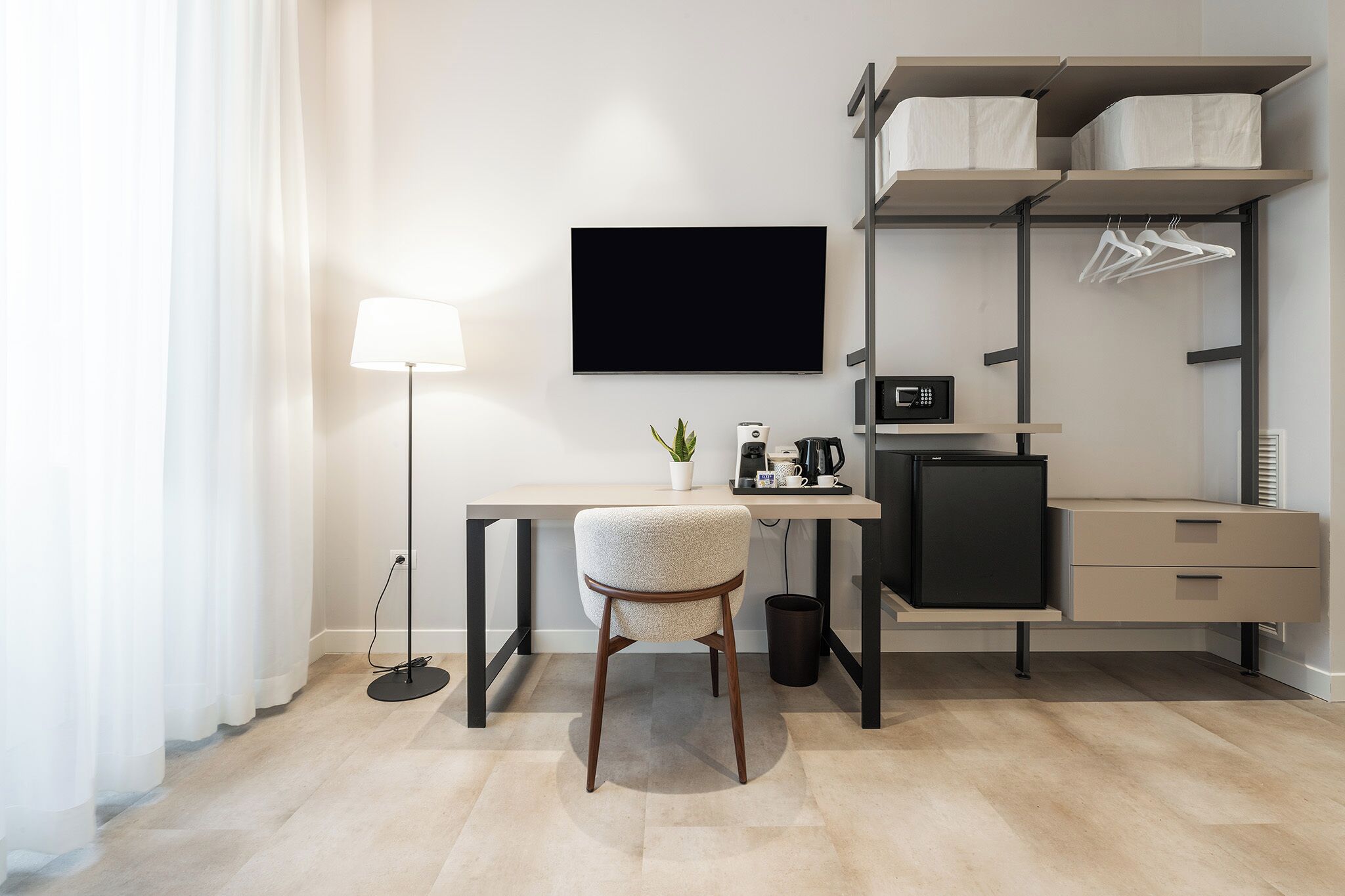 Habitación de hotel moderna con escritorio, silla, televisor de pantalla plana, cafetera, microondas y armario empotrado con espacio para colgar.