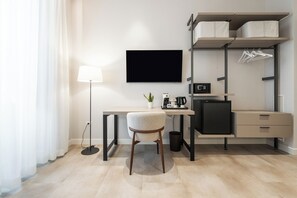 A modern hotel room with a desk, chair, flat-screen TV, coffee machine, microwave, and built-in wardrobe with hanging space.