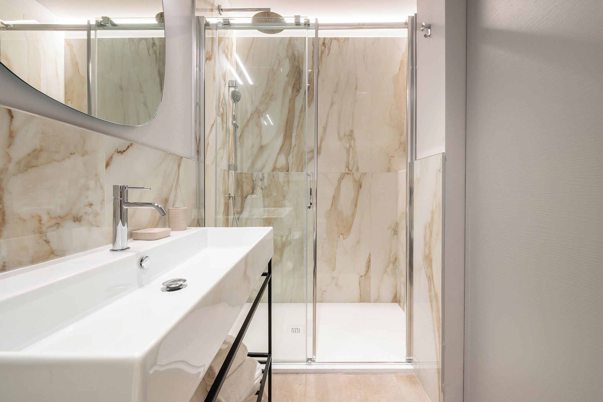 A modern bathroom with a glass-enclosed shower, a white sink, and marble walls.