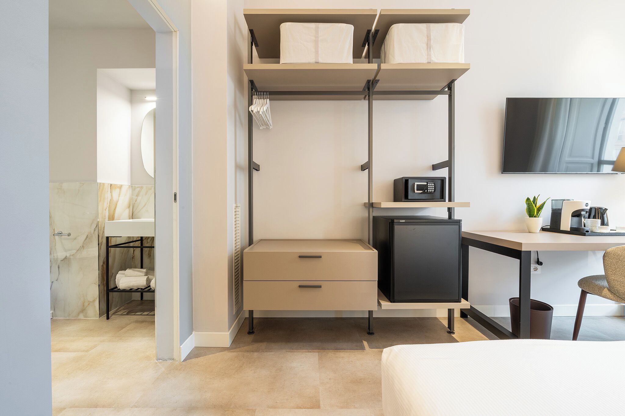 Una habitación pequeña con cama, escritorio con computadora, refrigerador y televisor.