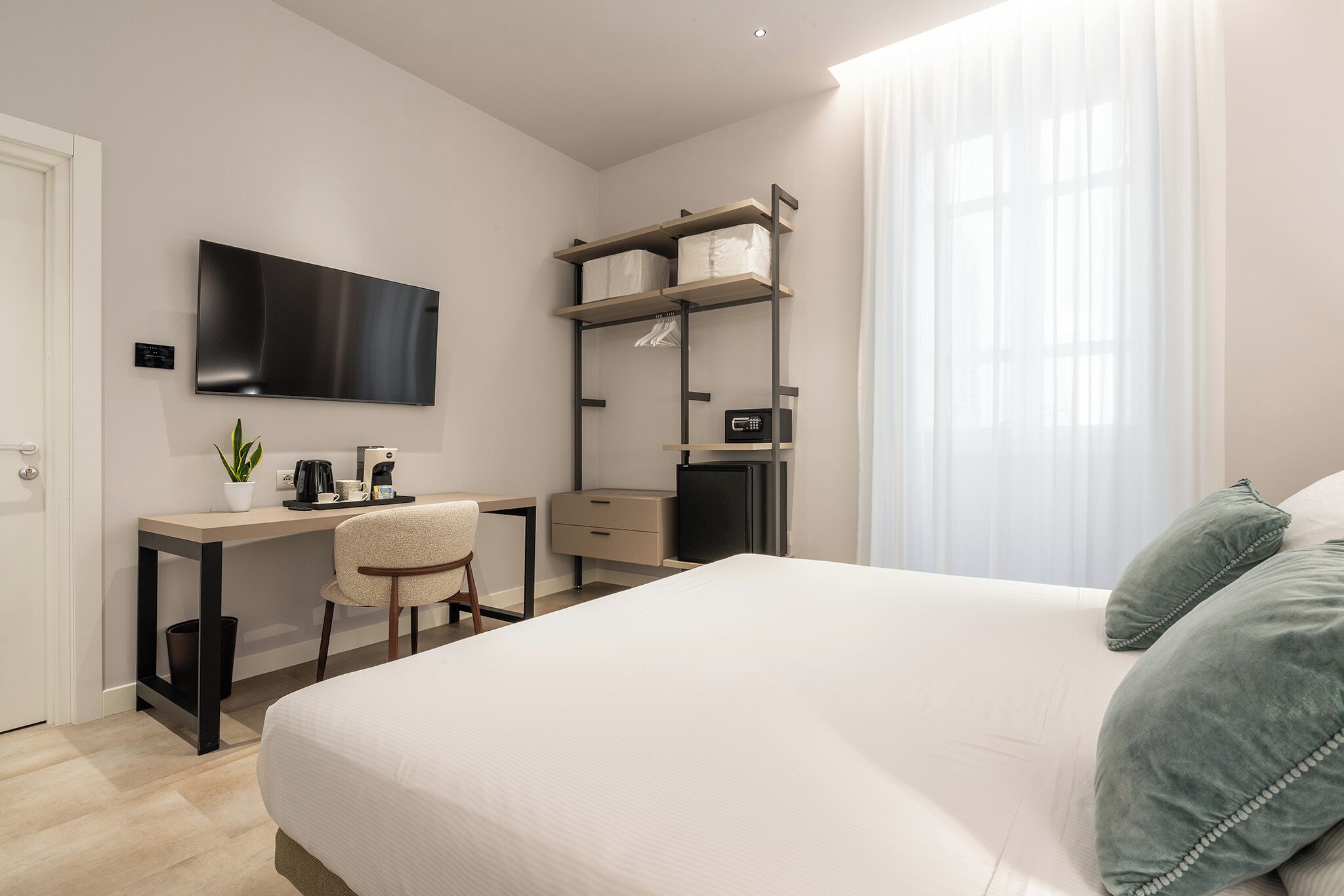 Ein modernes Hotelzimmer mit einem Bett, einem Schreibtisch, einem Sessel, einem Fernseher und einem Kleiderschrank.