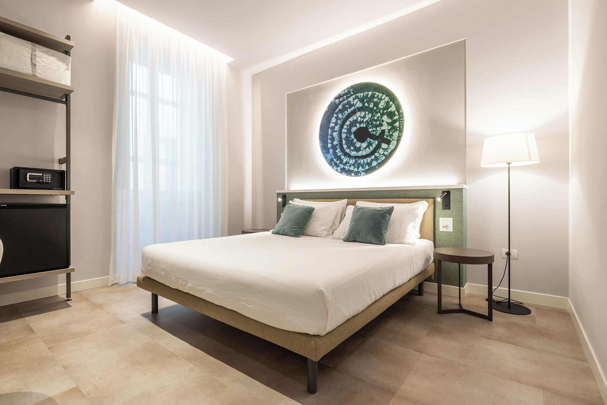 A hotel room with a bed, bedside table, lamp, and a wall-mounted artwork.