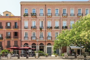 A multi-story building with balconies, a street cafe, and a tree in the foreground.