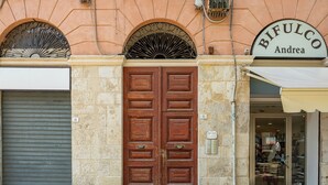 Fachada de edificio con una puerta de madera grande, un letrero que dice 'BIFULCO Andrea' y la entrada de una tienda con puerta de cristal.