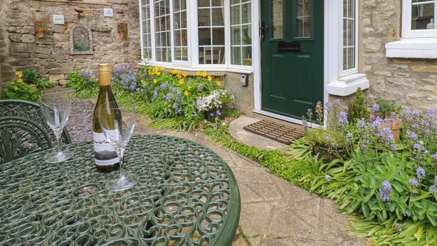 A stone building with a green door, a window with a white frame, and a small garden with flowers. - Wedgewood Cottage (Leyburn)