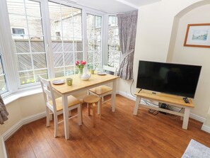 A room with a wooden dining table, chairs, a television on a stand, and a window with curtains. - Wedgewood Cottage (Leyburn)