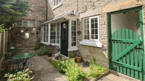 A stone building with a green door, a small garden with potted plants, and a table and chairs outside. - Wedgewood Cottage (Leyburn)