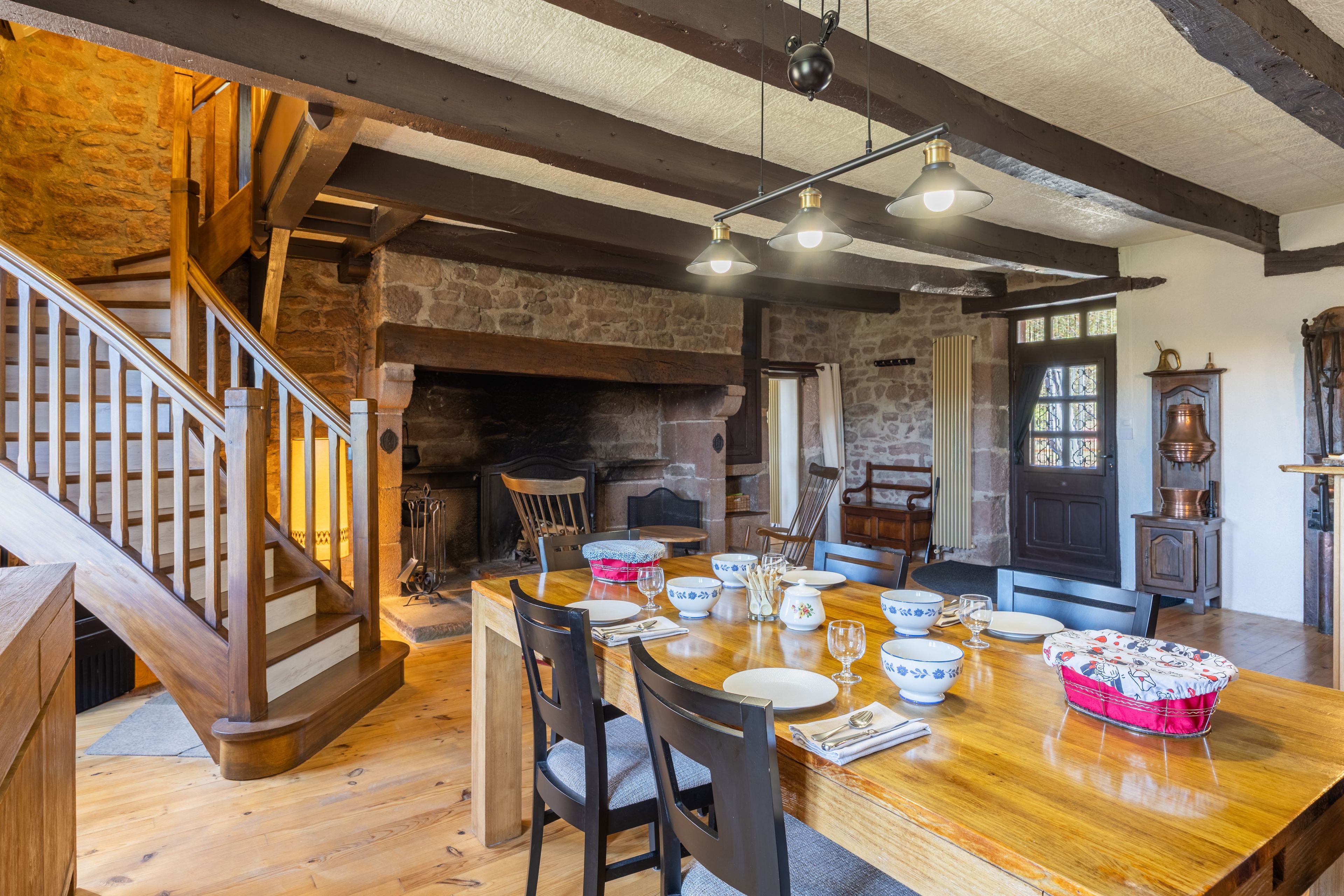 A dining area with a wooden table set for four, surrounded by chairs, in a room with exposed beams and stone walls.