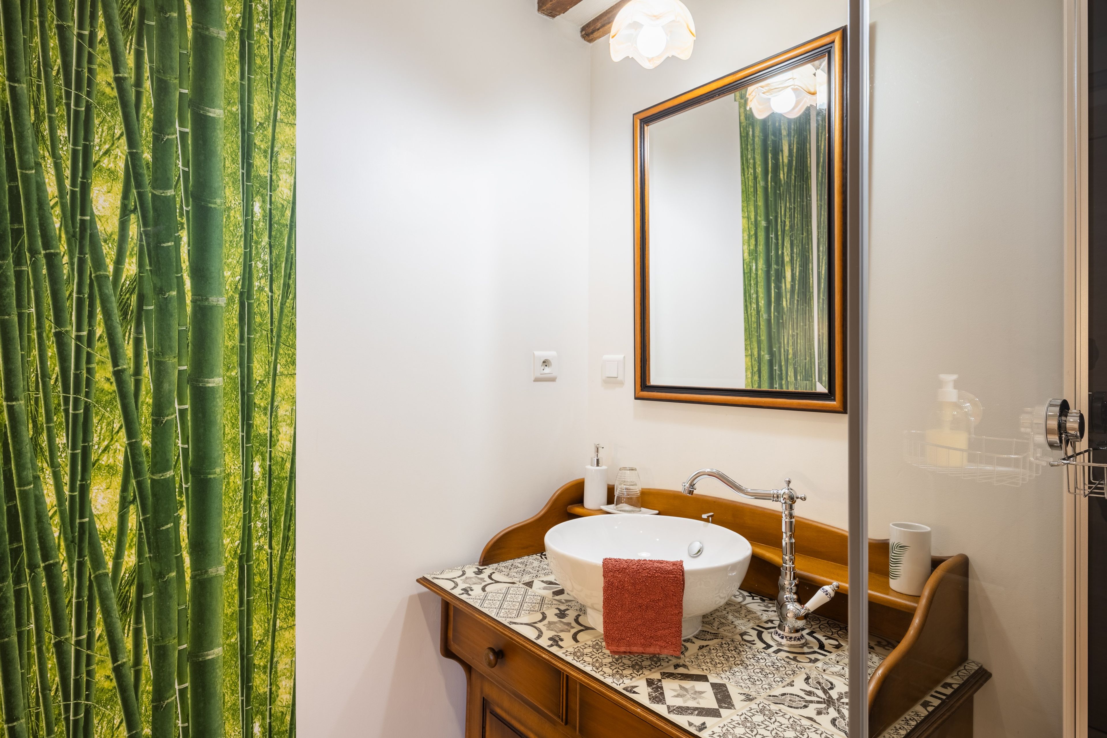 Un baño con tocador de madera, un lavabo blanco, un espejo y una cortina de bambú.