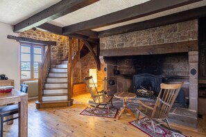 A rustic interior with a stone fireplace, wooden staircase, and a dining area.