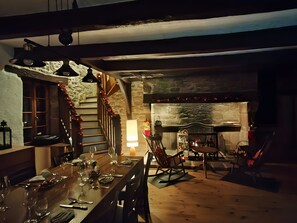 A cozy dining area with a stone fireplace, wooden staircase, and a dining table set for four. - “Sans Chichi Chambres Et Table” Guesthouse with Shared Terrace, Garden, and Wi-Fi (Escandolières)