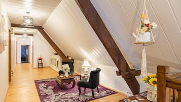Ett rum i loftstil med synliga träbjälkar, en svart fåtölj, ett träbord och en hängande lampa i makramé.