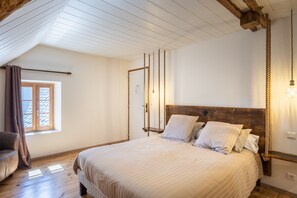 Ein Schlafzimmer mit hölzernem Kopfteil, einem Bett mit weißer Bettwäsche, einem Fenster mit Vorhängen und einem Holzboden.