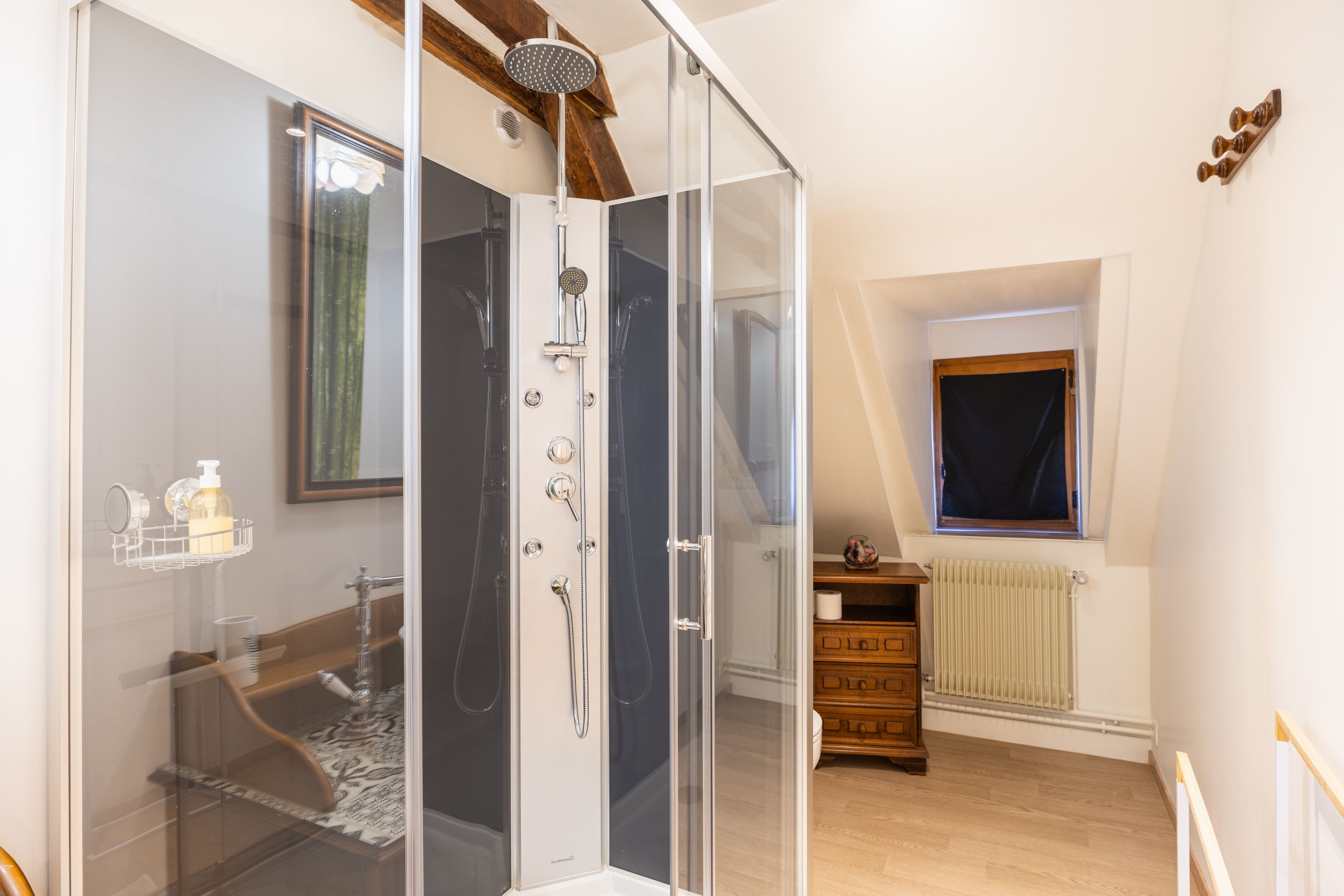Een moderne badkamer met een douchecabine van glas, een houten vloer, een radiator en een raam met uitzicht.