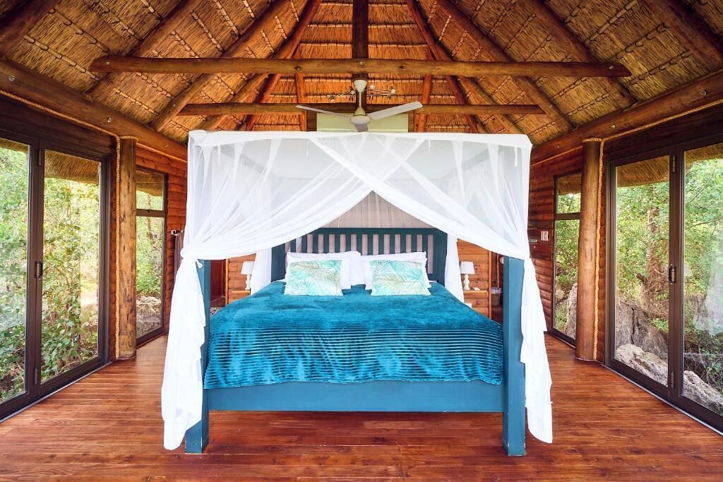 A room with a bed under a canopy, wooden walls, and large windows.