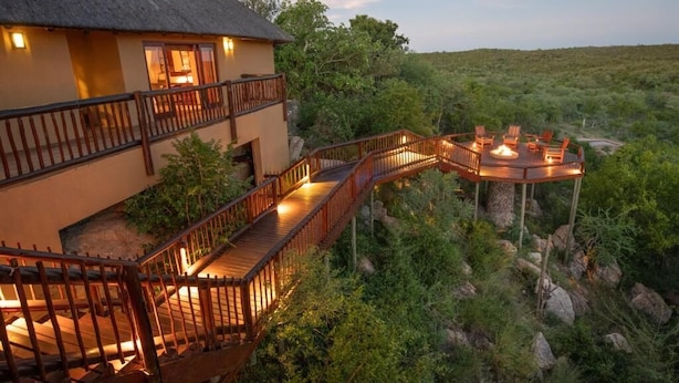 A two-story building with a thatched roof, wooden balconies, and a wooden deck with chairs and a fire pit. - Parsons House (Hoedspruit)