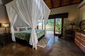 Ein Schlafzimmer mit Himmelsbett, Nachttisch, Schminktisch und Spiegel, mit Blick ins Freie.
