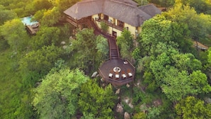 A large, two-story building surrounded by dense greenery, with a circular deck and a staircase leading to the upper level. - Parsons House (Hoedspruit)