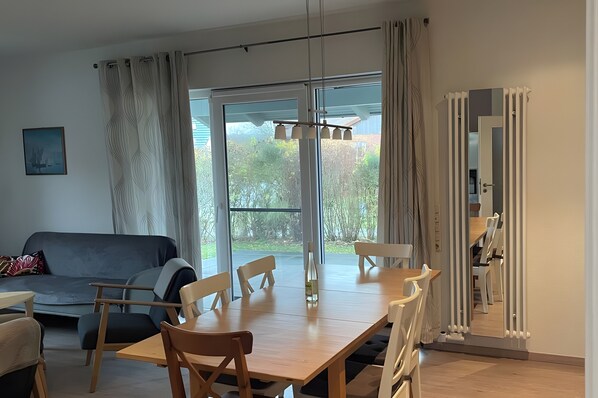 Un salon moderne comprenant un canapé, une table à manger, des chaises et une grande fenêtre avec des rideaux.