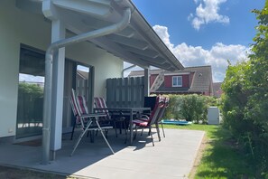 Une terrasse extérieure avec une table et des chaises, un espace abrité et une vue sur la maison voisine.