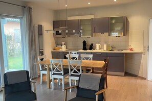 Une cuisine moderne avec un coin repas, dotée d’une grande fenêtre, de meubles gris et d’une table à manger en bois.