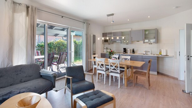 Un salon moderne comprenant un canapé, des fauteuils, une table à manger et un coin cuisine avec des placards et des appareils électroménagers.