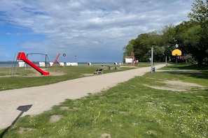 Ein Park mit einem Spielplatz, einem Basketballfeld und einem Weg zu einem Gewässer.