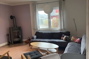 Un salon comprenant un canapé, une table ronde, une cheminée et une fenêtre donnant sur un bâtiment rouge.