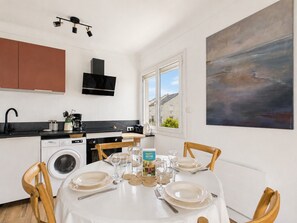 A modern kitchen with a washing machine, a dining area set for four with a table set for a meal, and a large abstract painting on the wall. - Near beach, flat 2 adults 2 children (Saint-Hilaire-de-Riez)