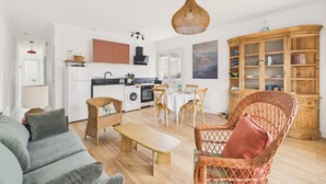 Ein modernes Wohnzimmer mit einer Couch, einem Couchtisch, Korbstühlen, einem Esstisch und einer Küche im Hintergrund.