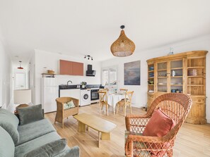 A modern living room with a sofa, a coffee table, wicker chairs, a dining table, and a kitchen in the background. - Near beach, flat 2 adults 2 children (Saint-Hilaire-de-Riez)