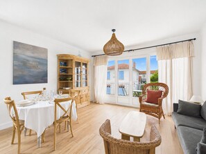 A dining area with a round table and chairs, a wicker sofa, a cabinet with glass doors, and a view through large windows. - Near beach, flat 2 adults 2 children (Saint-Hilaire-de-Riez)