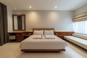 A modern hotel room with a large bed, a wooden desk, a bench, and a large mirror. - D' Green Nirava By Reccoma (Kabupaten Badung)