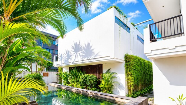 A modern building with a pool, surrounded by lush greenery and palm trees. - D' Green Nirava By Reccoma (Kabupaten Badung)