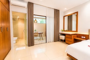 A modern hotel room with a glass shower enclosure, a wooden vanity with a mirror, and a bed with a white comforter.