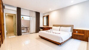 A modern hotel room with a large bed, a desk, and a shower area. - D' Green Nirava By Reccoma (Kabupaten Badung)