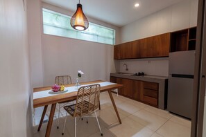 A modern kitchen with wooden cabinets, a stainless steel refrigerator, and a dining table with a chair. - D' Green Nirava By Reccoma (Kabupaten Badung)