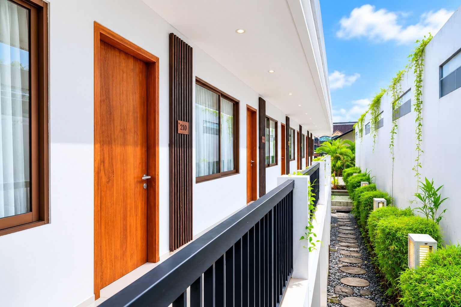 A row of hotel rooms with wooden doors, a balcony, and a garden pathway.